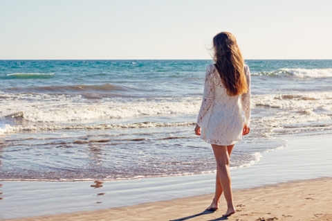 Woman walking on sand towards the ocean